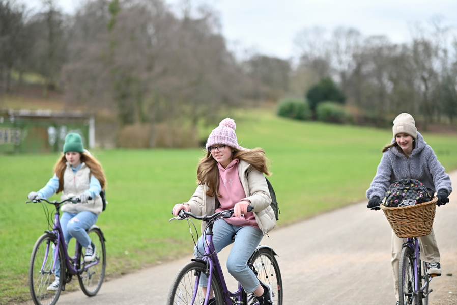 Three girls cycle together in a park in winter