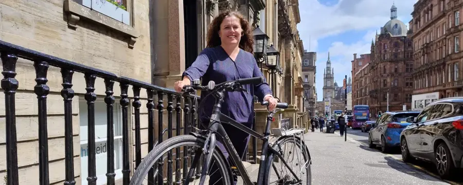 Clare stands with a bike on a city centre street in Glasgow