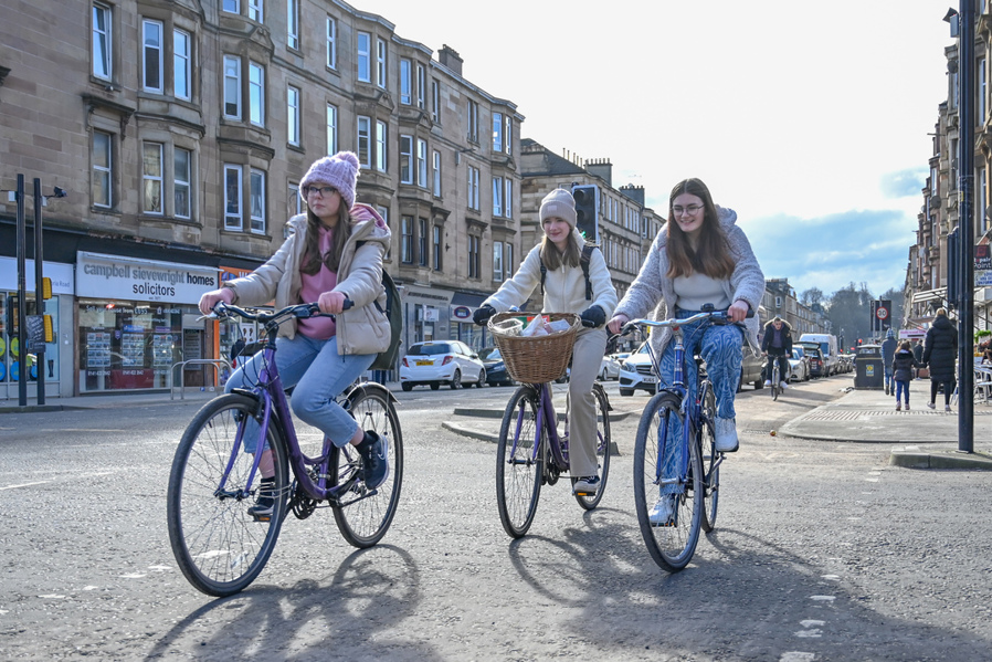 Three girls cycle together along the South City Way protected cycle route on Victoria Road in Glasgow