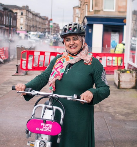 Woman wearing helmet standing with bike next to urban cycle route