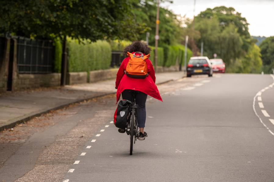 A woman in a red coat cycles on-road away from the viewer