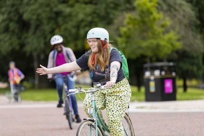 A woman signals as she rides her bike during an adult cycle training session