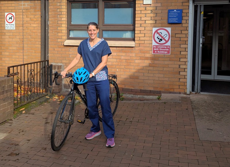 NHS health visitor Kirsty, pictured smiling with her bike outside the health centre where she works