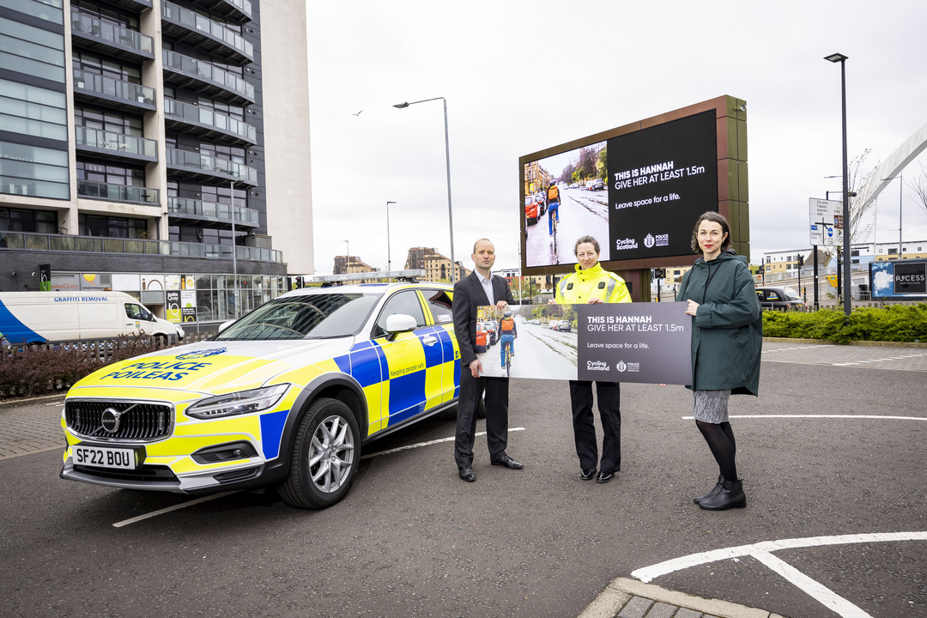 Staff from Police Scotland and Cycling Scotland display a Give Cycle Space banner in front of the campaign billboard