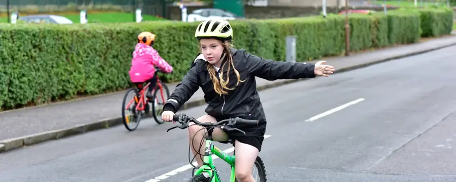 A girl signals with her left hand while riding a bike on road, as part of a Bikeability Scotland cycling training session